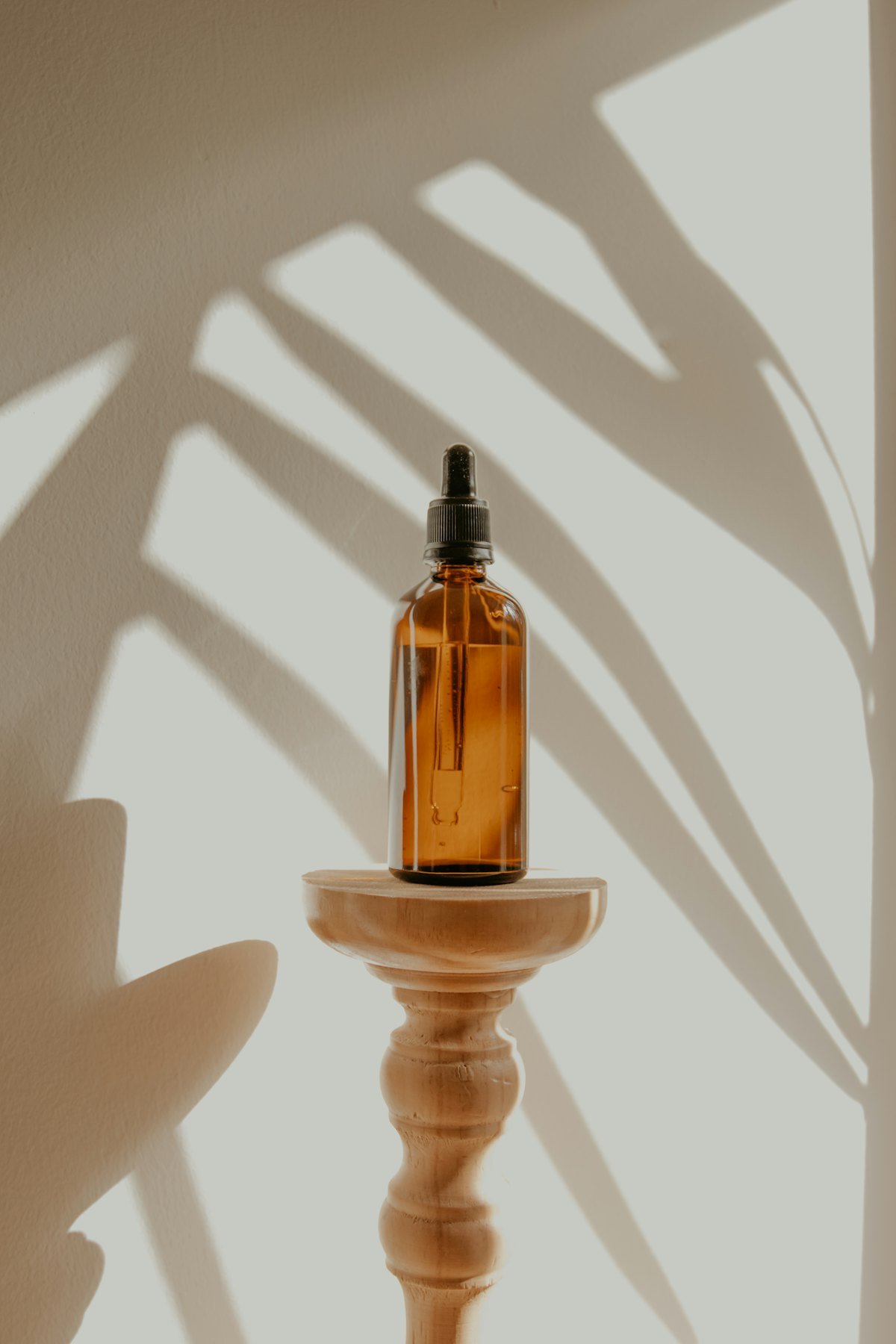 An amber glass dropper bottle standing on a small wooden stand in sunlight