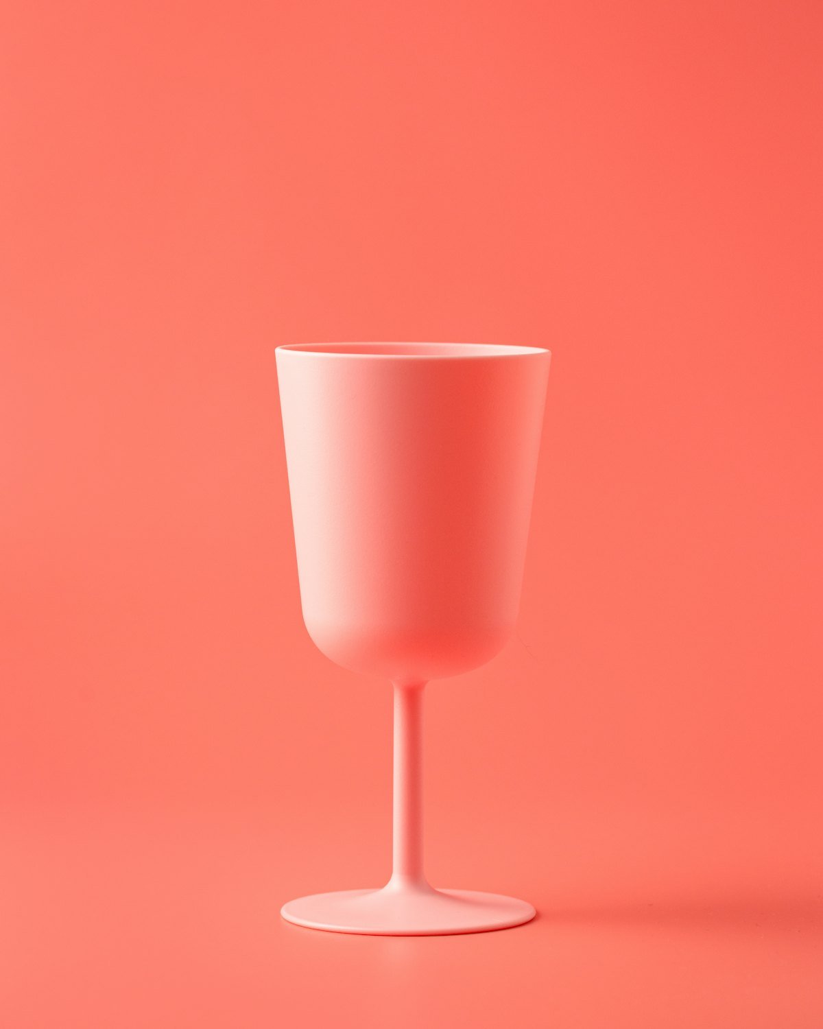 A single pale pink drinking cup against a coral background