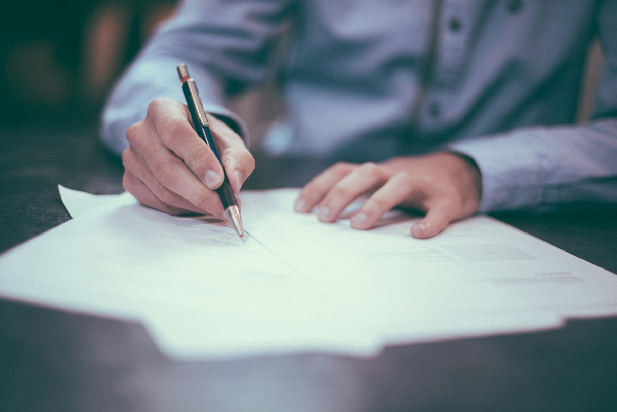 A person writing with a pen on a printed sheet of paper