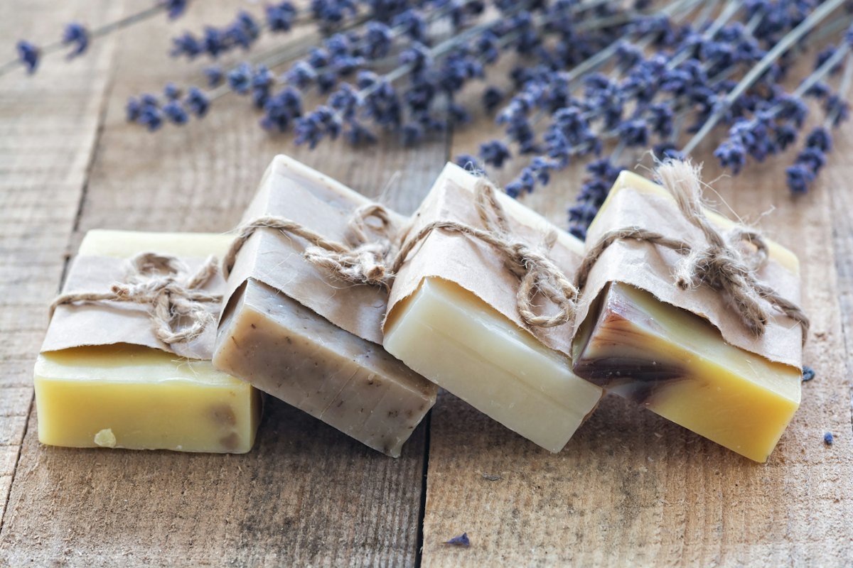 Four bars of soap wrapped in paper and tied with string on a wooden table, with lavender behind them